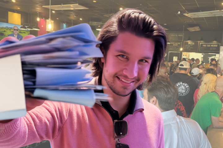 Jake Maines smiling while holding event materials in front of a large crowd at Networking Happy Hour.