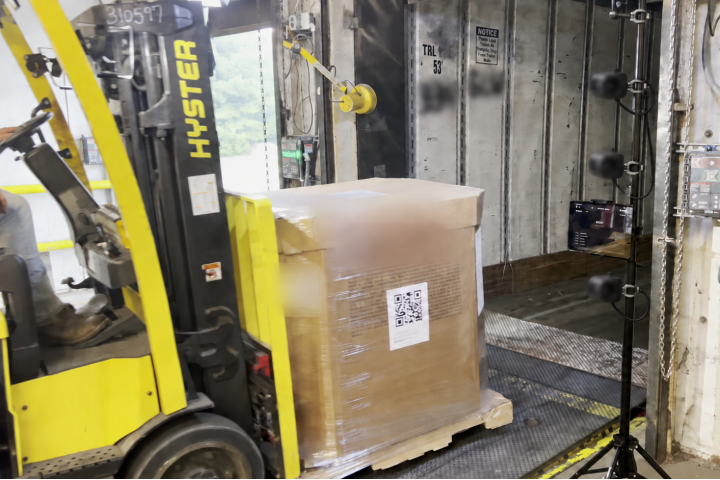 A forklift moves a pallet with a QR code through a warehouse dock door beside Flowtally cameras.